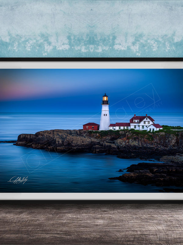 A framed photograph of a lighthouse on a rocky coastline, with the ocean and a colorful sky in the background.