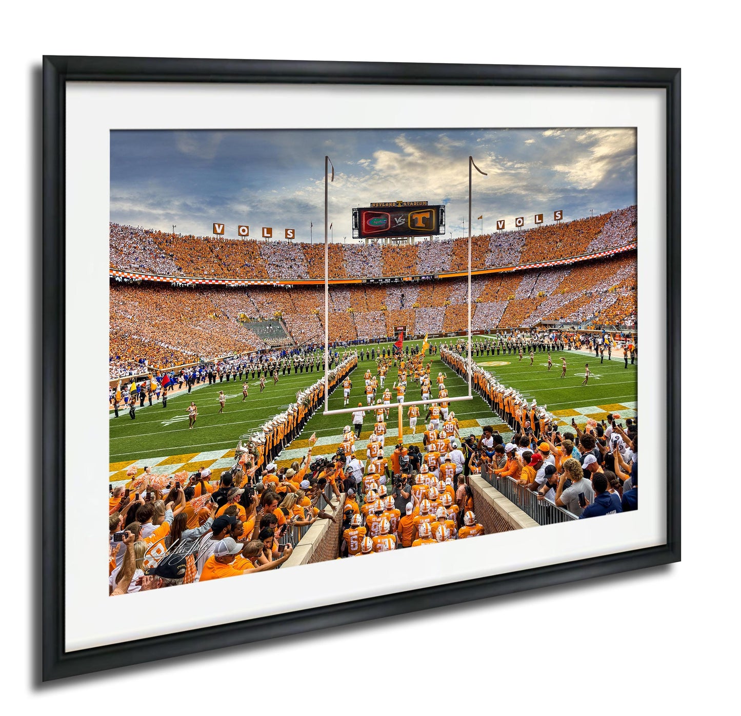 A framed photograph of a football game in progress, with a large crowd of spectators filling the stands and players on the field.