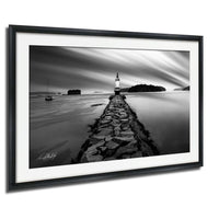A black and white photograph of a lighthouse on a rocky pier, with a small boat visible in the distance.