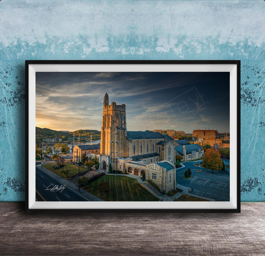 A framed photograph of a large, ornate building with a tower, likely a church, set against a backdrop of a city skyline at sunset.