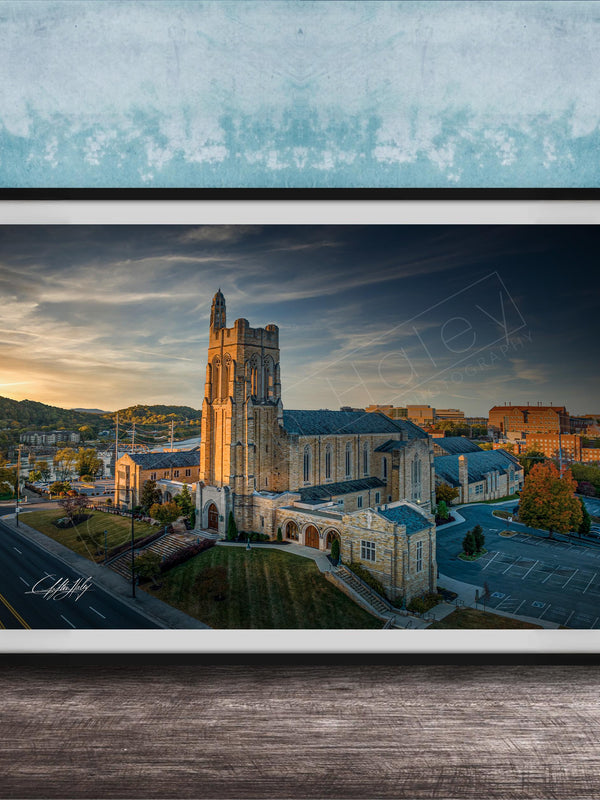 A framed photograph of a large, ornate building with a tower, likely a church, set against a backdrop of a city skyline at sunset.