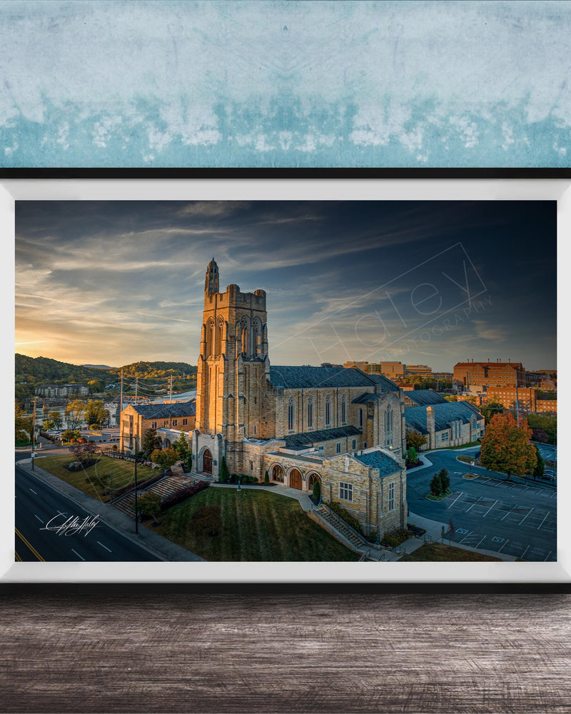 A framed photograph of a large, ornate building with a tower, likely a church, set against a backdrop of a city skyline at sunset.