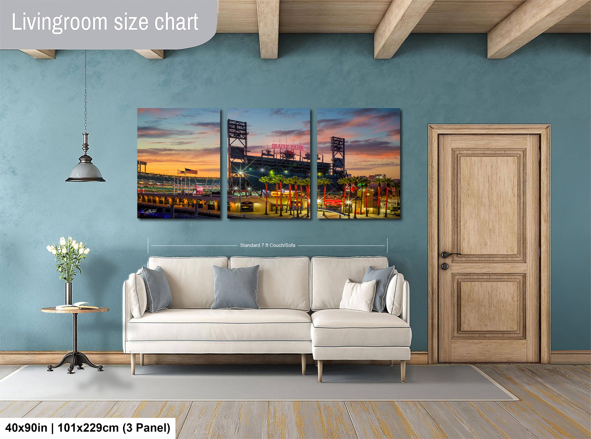 The image is a living room with a large wall art depicting a city skyline at sunset. The wall art is divided into three panels, each showing a different part of the cityscape. The living room has a white sofa and a wooden door, and the floor is covered with a gray rug.