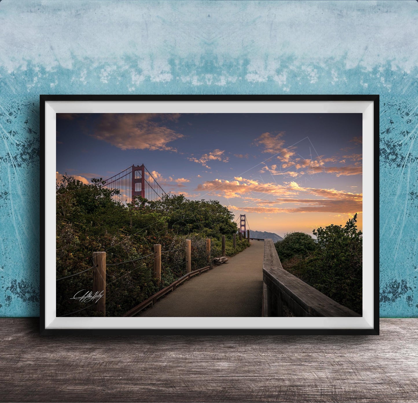 A framed photograph depicting a scenic view of the Golden Gate Bridge at sunset, with a wooden walkway leading towards the bridge and a colorful sky in the background.