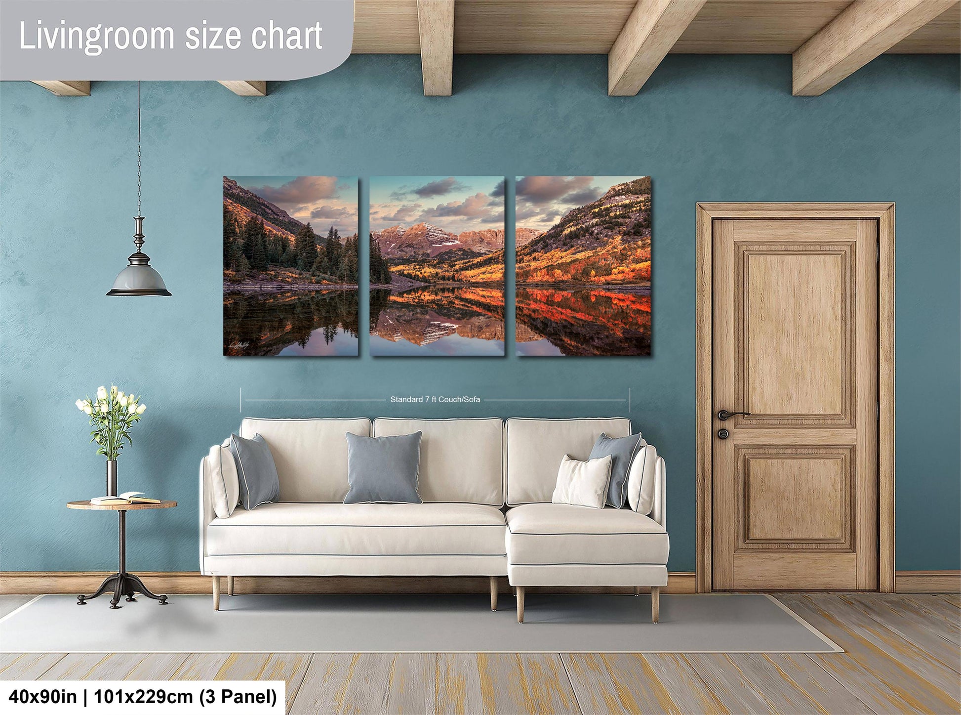 The image is a living room with a large, three-panel landscape painting hanging on the wall. The painting depicts a scenic mountain landscape with a lake and trees. The room has a white sofa and a wooden door, creating a cozy and inviting atmosphere.