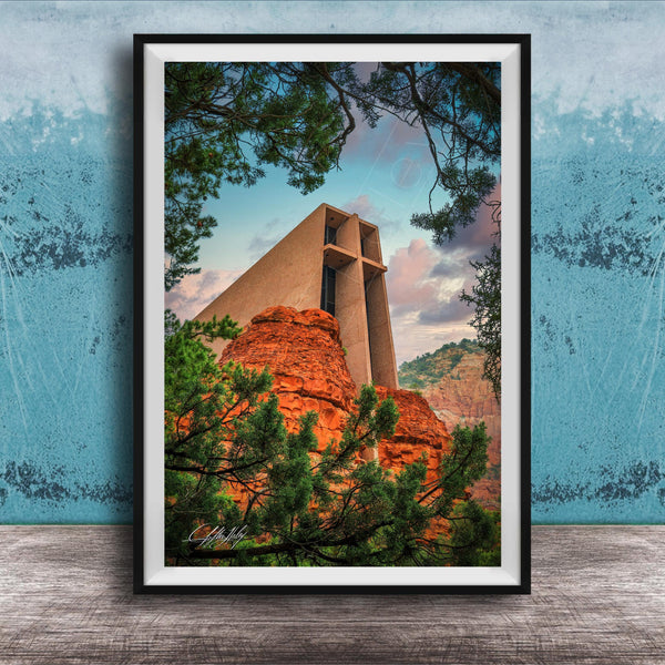 A framed photograph of a large, modern church with a distinctive cross-shaped roof, set against a backdrop of red rock formations and lush greenery.