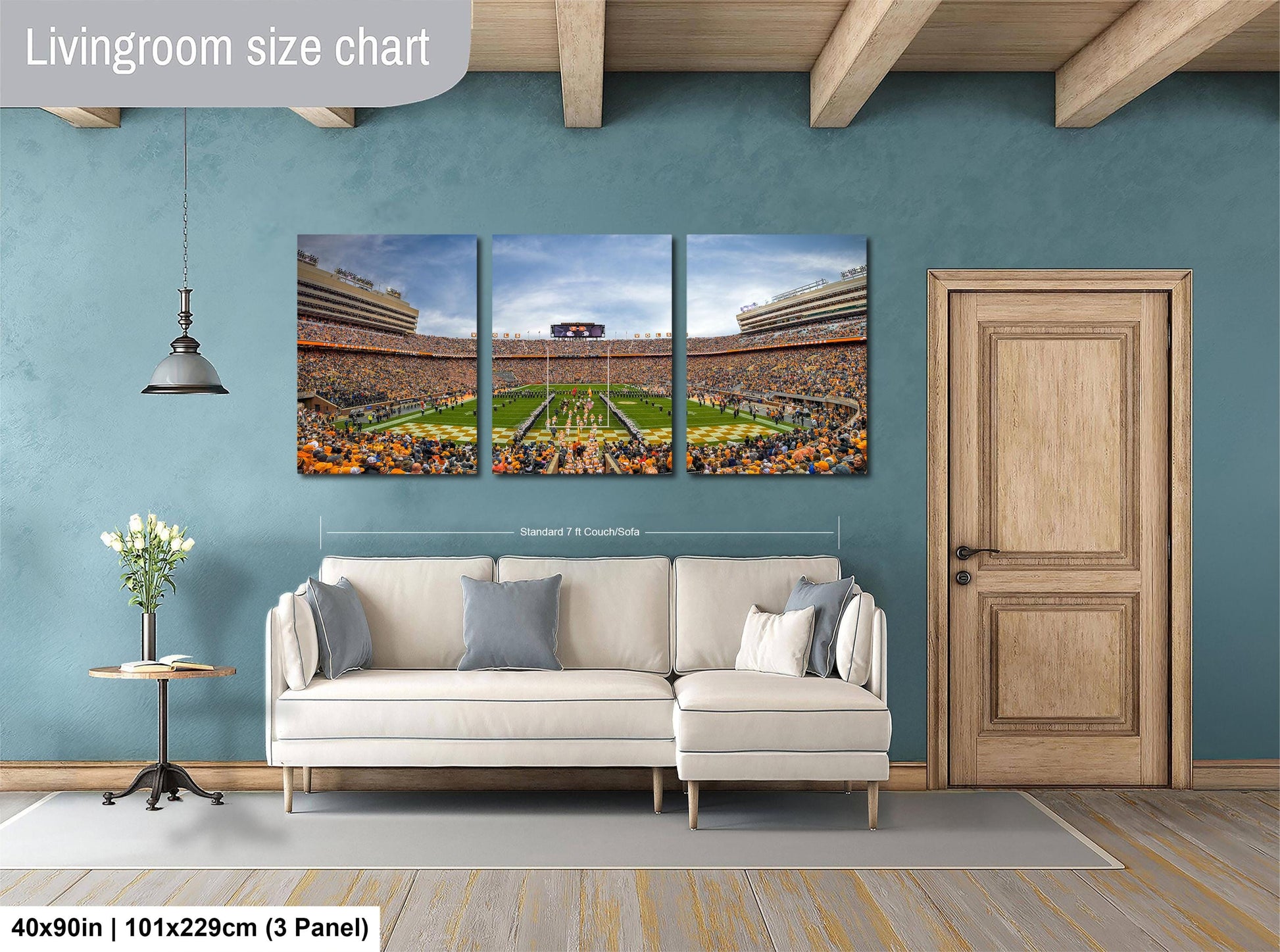 The image is a living room with a large wall-mounted painting depicting a football stadium. The painting is divided into three panels, showing different aspects of the stadium. The room has a white sofa, a wooden door, and a small table with a vase of flowers. The painting is approximately 40 inches wide and 101.29 cm tall, with a 3-panel layout.