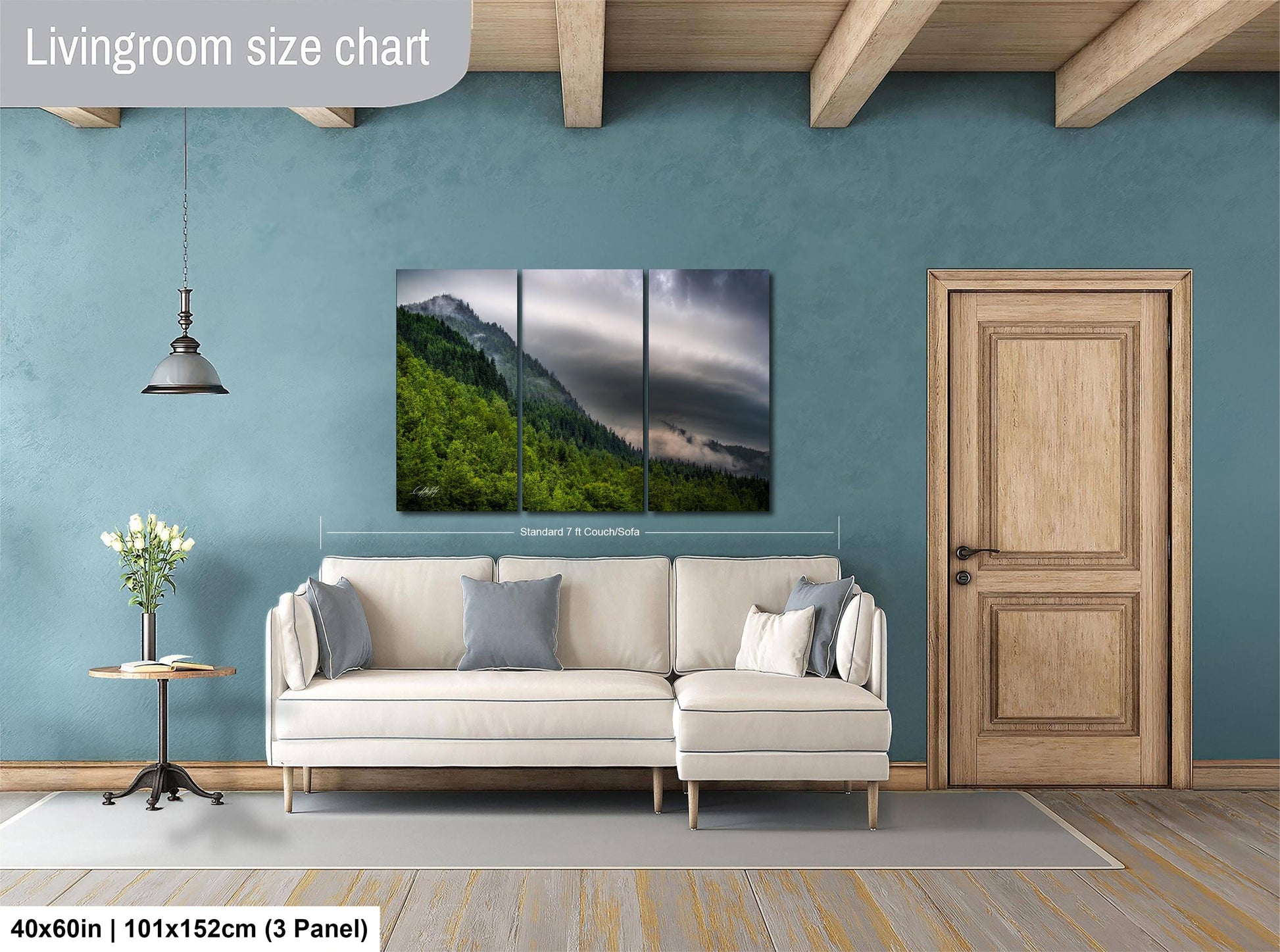 The image is a living room with a large painting of a mountain landscape hanging on the wall. The painting is divided into three panels, and the living room has a white sofa, a wooden door, and a small table with a vase of flowers.