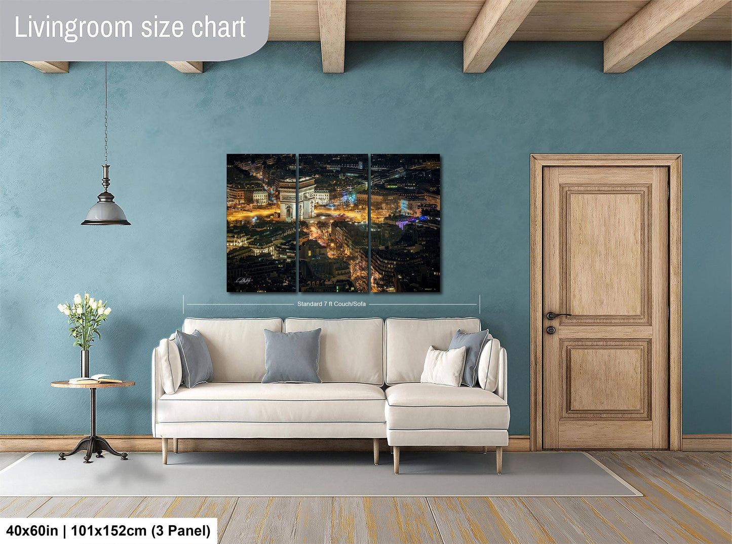 The image is a living room with a large, multi-panel, high-resolution painting of a cityscape hanging on the wall. The painting is framed in a wooden frame and is displayed on a wall above a white sofa. The room has a wooden door and a small table with a vase of flowers. The living room appears to be well-lit and spacious, with a cozy and inviting atmosphere.
