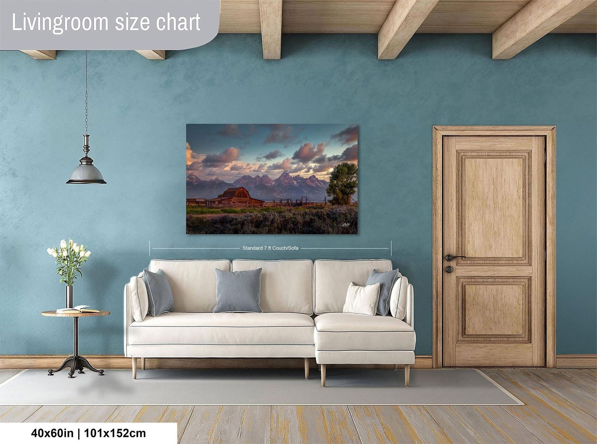 a living room with a large painting of a mountain landscape hanging on the wall. The painting is framed and measures 40 inches by 101.5 centimeters. The room has a white sofa and a wooden door, creating a cozy and inviting atmosphere.