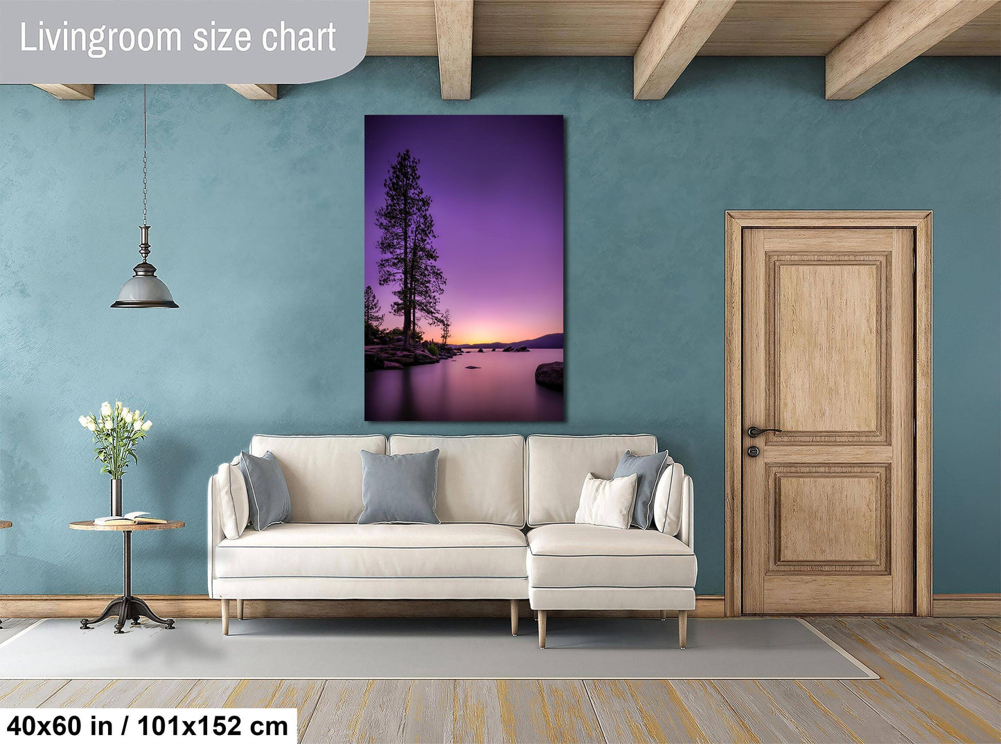 a living room with a large wall painting of a serene landscape featuring a tree and a body of water at sunset. The room has a white sofa, a wooden door, and a wooden table with a vase of flowers. The painting is hung above the sofa, and the wall is painted in a light blue color.
