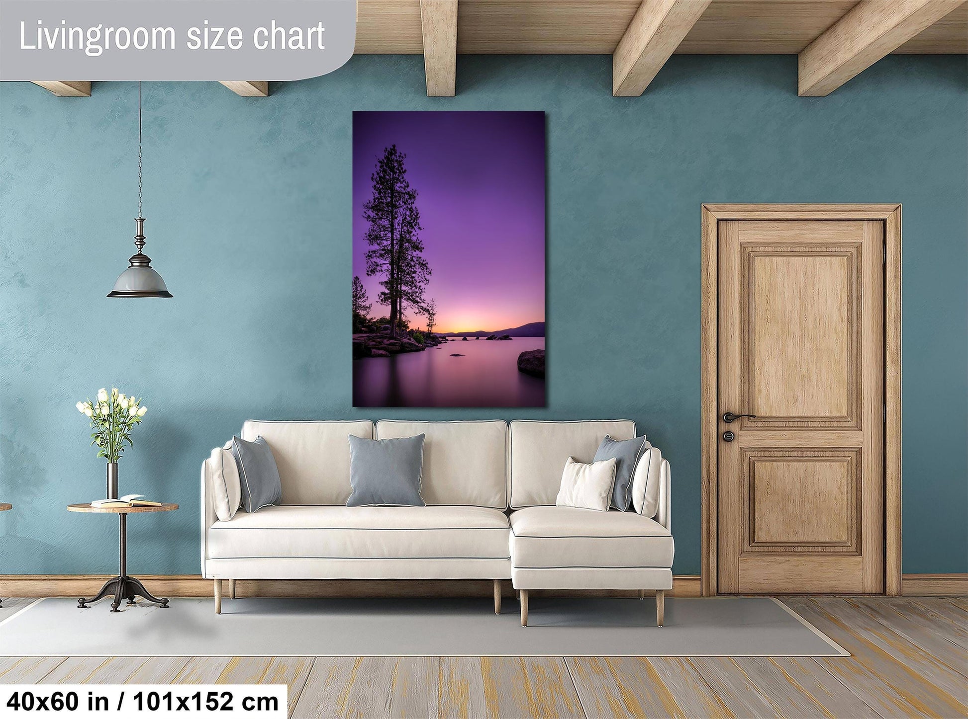a living room with a large wall painting of a serene landscape featuring a tree and a body of water at sunset. The room has a white sofa, a wooden door, and a wooden table with a vase of flowers. The painting is hung above the sofa, and the wall is painted in a light blue color.