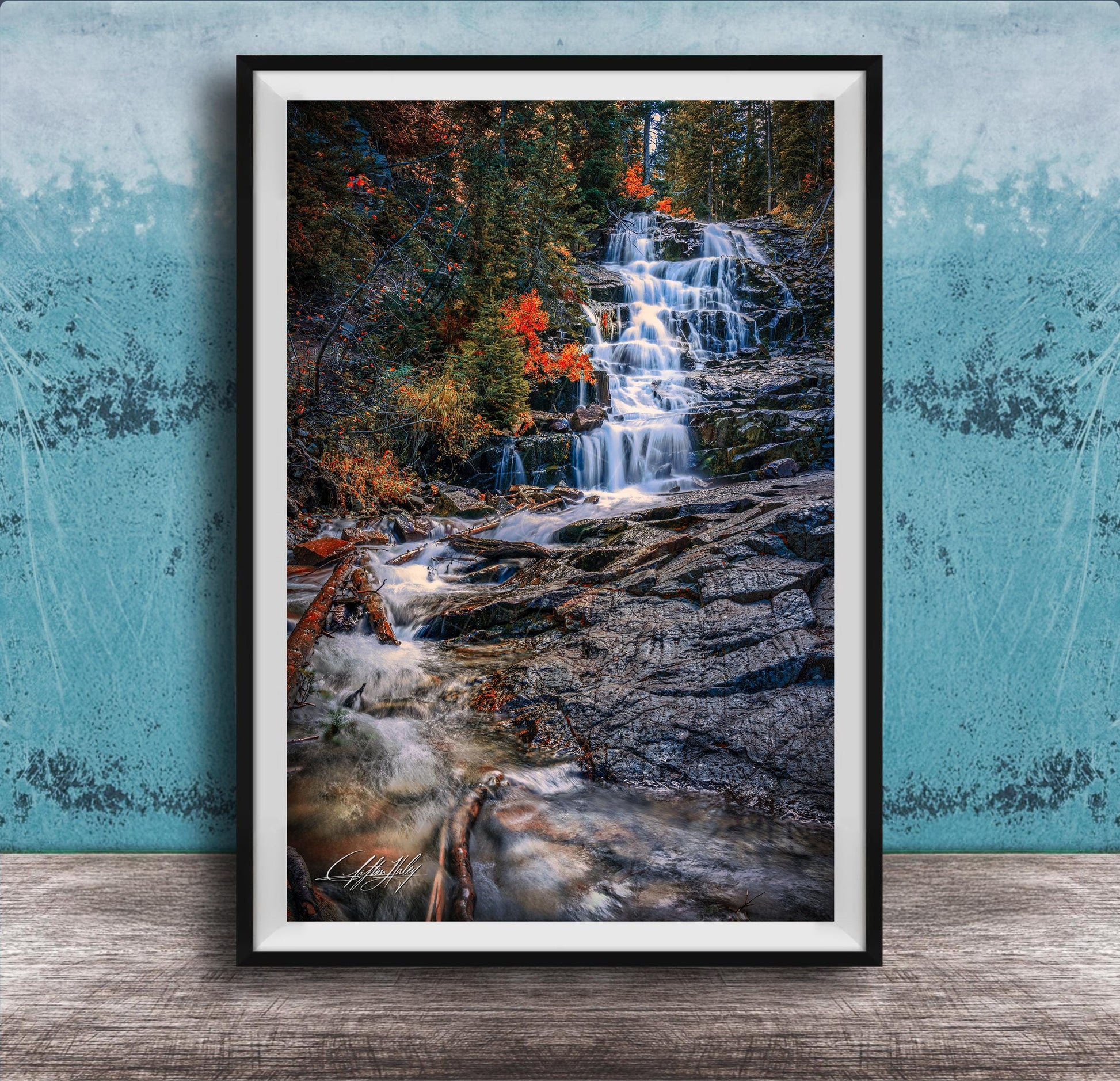 A framed photograph of a waterfall cascading down a rocky cliff surrounded by vibrant autumn foliage.