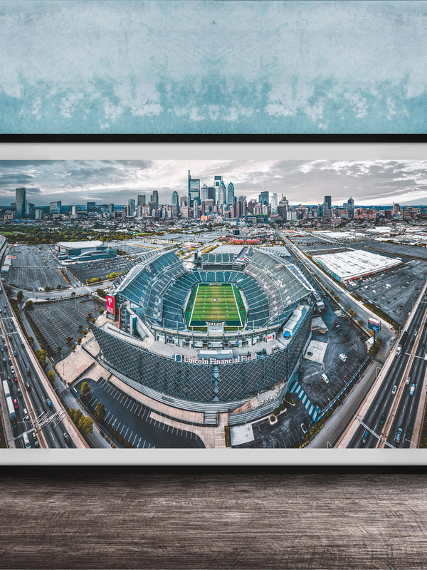 An aerial view of a large sports stadium surrounded by a city skyline, with the stadium's field and surrounding parking lots visible.