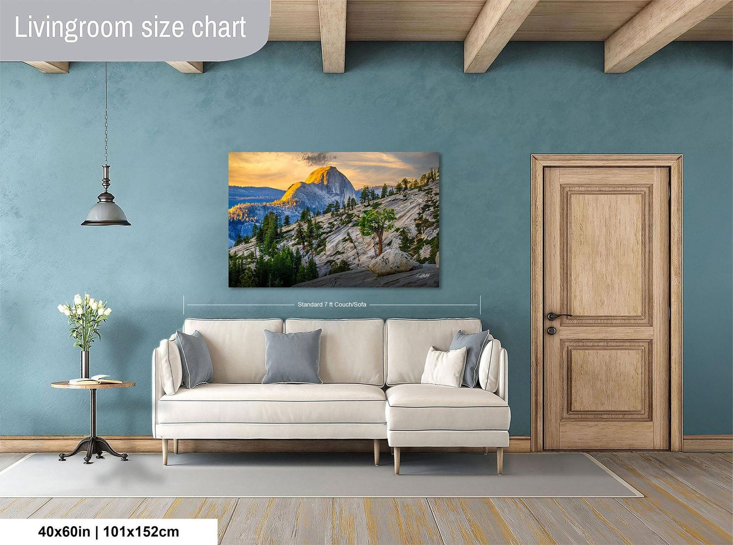 a living room with a large, framed landscape painting hanging on the wall. The painting features a mountain landscape with a sunset. The room has a white sofa and a wooden door, and there is a vase of flowers on a table. The painting is approximately 40 inches wide and 115 centimeters tall.