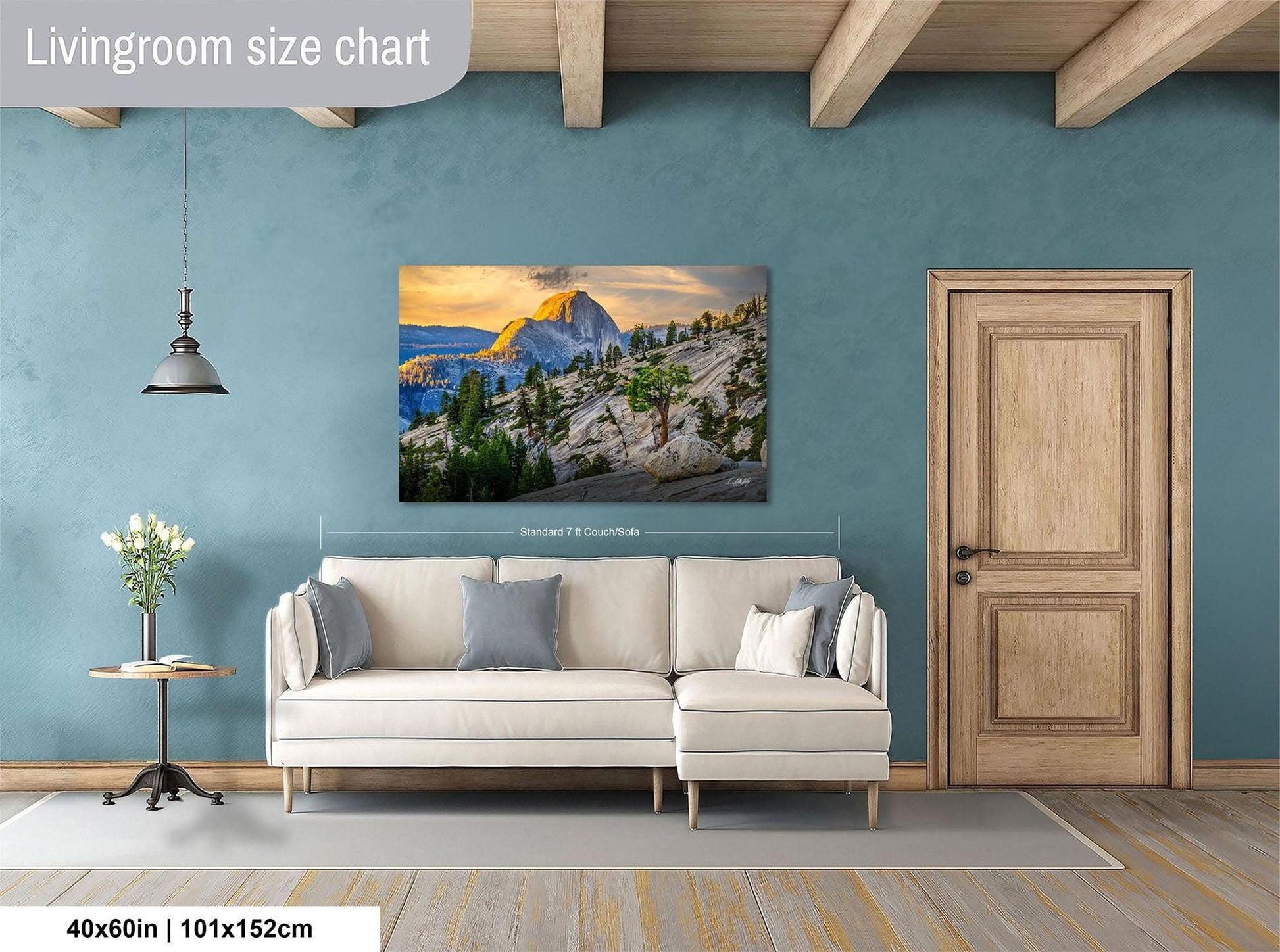 a living room with a large, framed landscape painting hanging on the wall. The painting features a mountain landscape with a sunset. The room has a white sofa and a wooden door, and there is a vase of flowers on a table. The painting is approximately 40 inches wide and 115 centimeters tall.