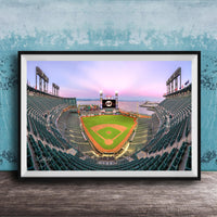 A framed photograph of a baseball stadium at dusk, with the field illuminated and the sky displaying a colorful sunset.