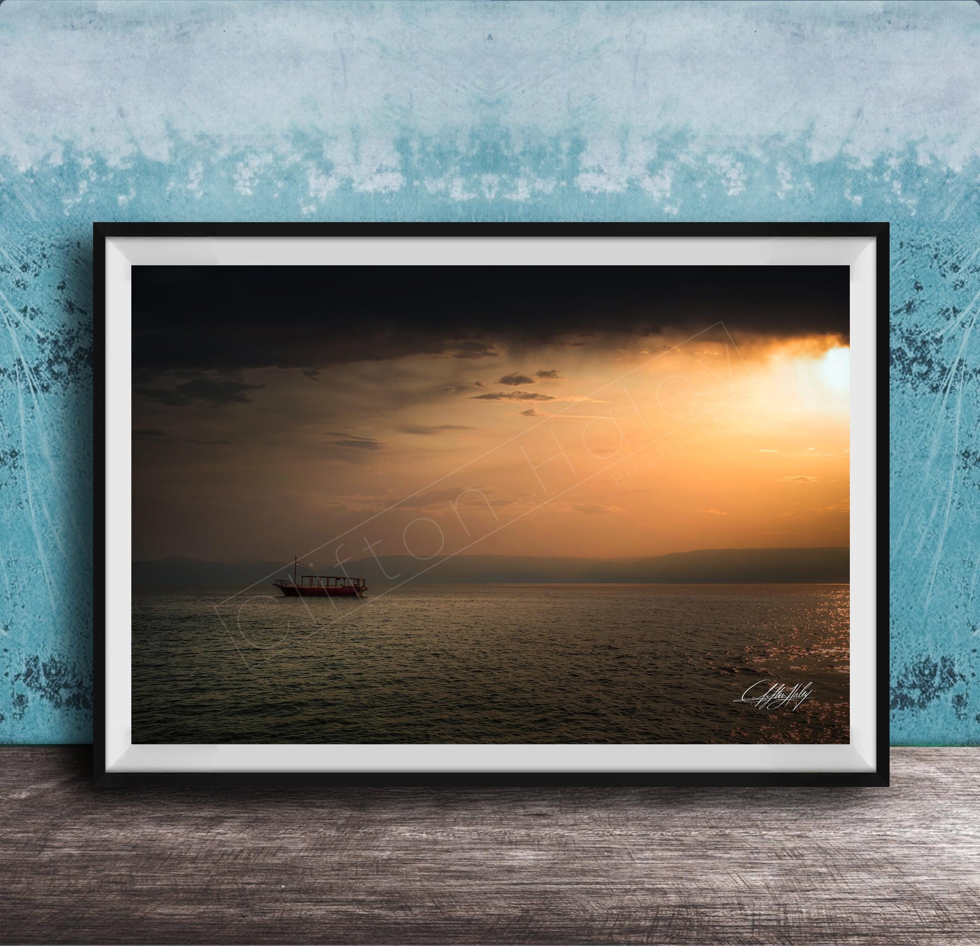A framed photograph of a boat sailing on a calm body of water at sunset, with a blue sky and clouds in the background.