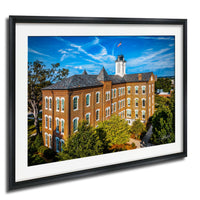 A large brick building with a clock tower, surrounded by trees and a blue sky with wispy clouds.