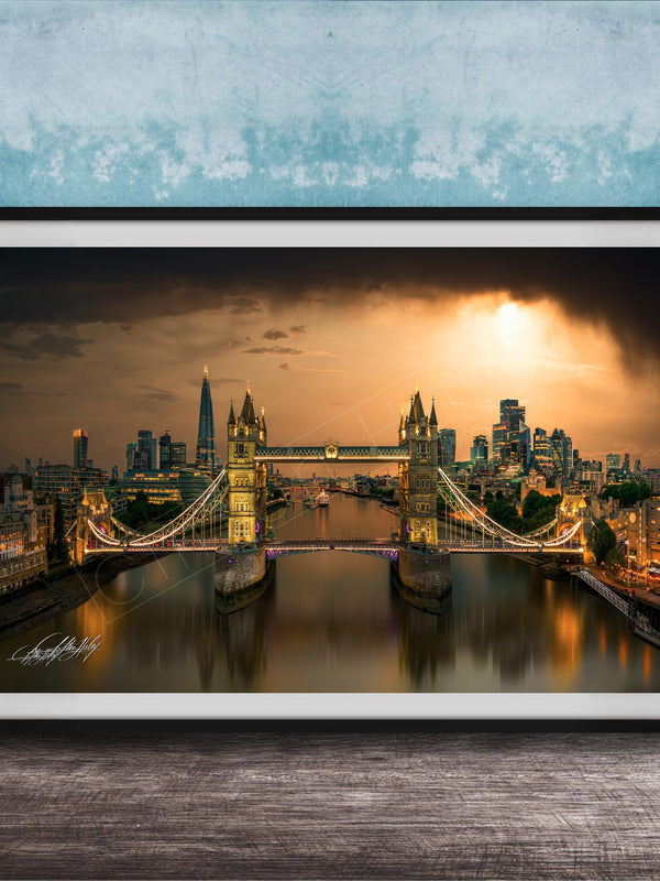 A framed photograph of the Tower Bridge in London, England, with the city skyline and the River Thames in the background, illuminated by a warm, golden glow.