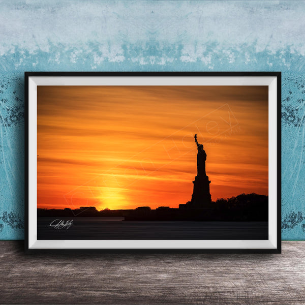A framed photograph of the Statue of Liberty silhouetted against a vibrant sunset sky.