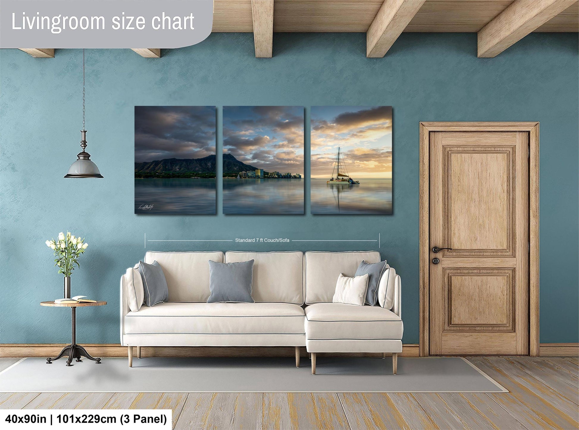 The image is a living room with a white sofa and a wooden door. Above the sofa, there is a triptych of landscape paintings depicting a serene scene with mountains, a sailboat, and a sunset. The paintings are framed and hung on the wall, creating a harmonious and visually appealing interior design.