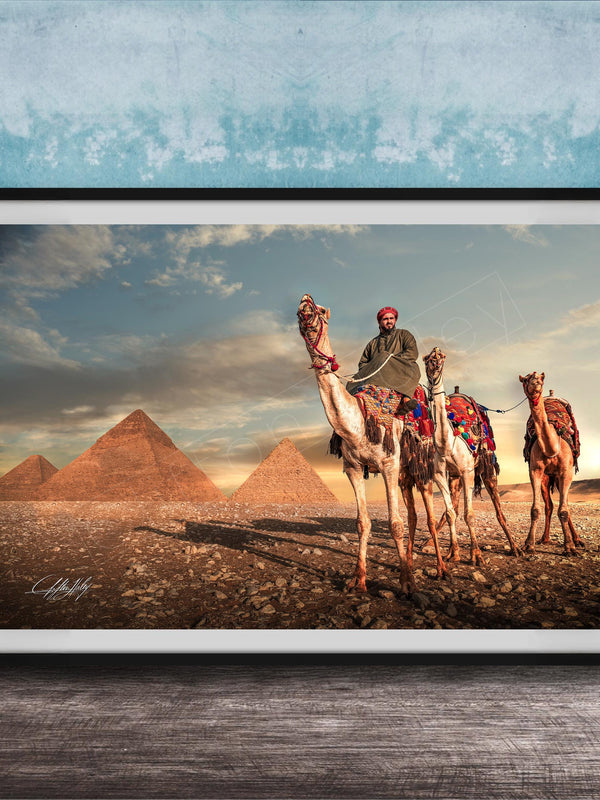 A framed photograph depicting a camel caravan in front of the iconic pyramids of Giza, Egypt, with a man riding one of the camels.