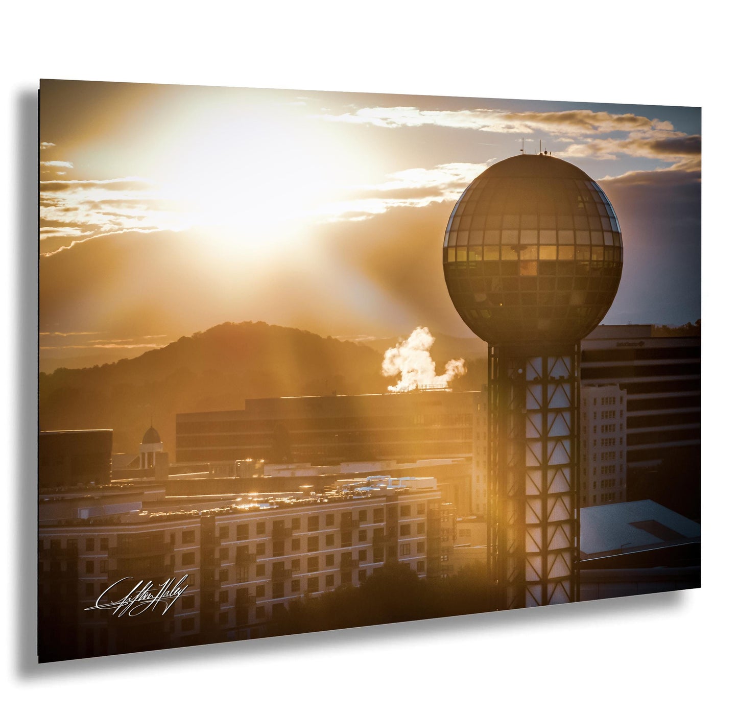a city skyline at sunset, with a large tower in the foreground and a mountain range in the background.