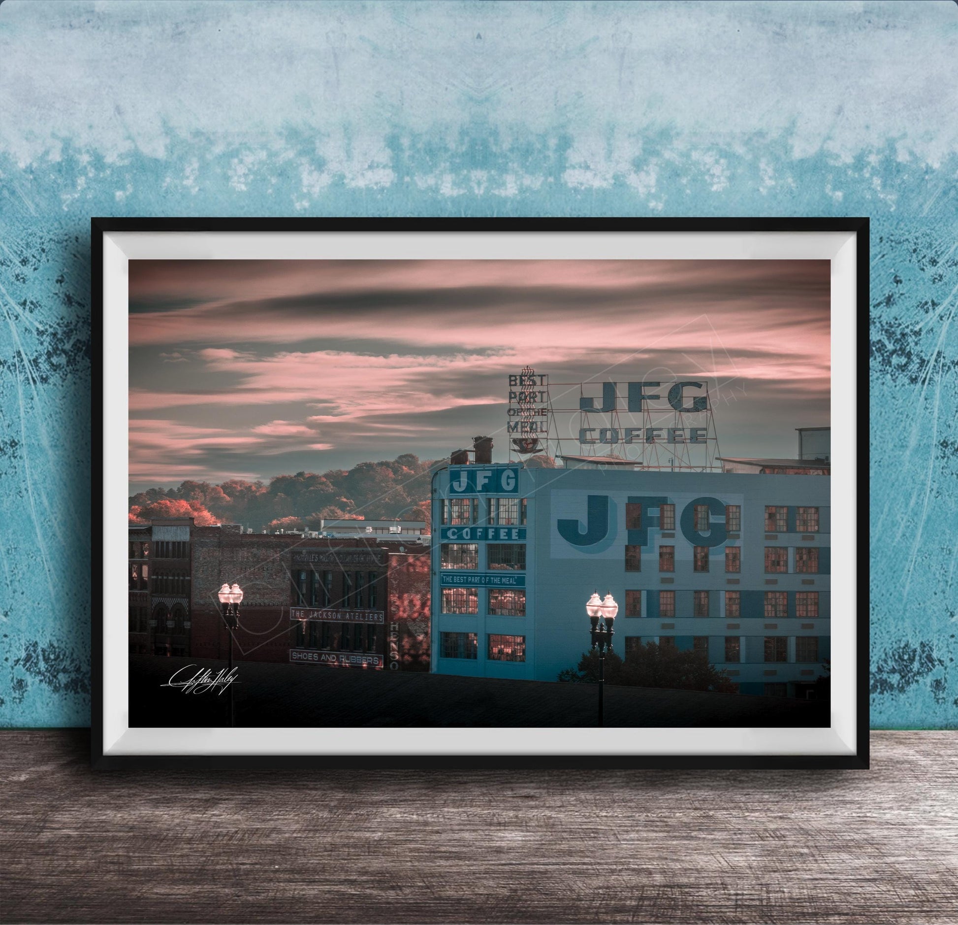 A framed photograph of a cityscape at sunset, with buildings and a sign for JFG Coffee prominently displayed.