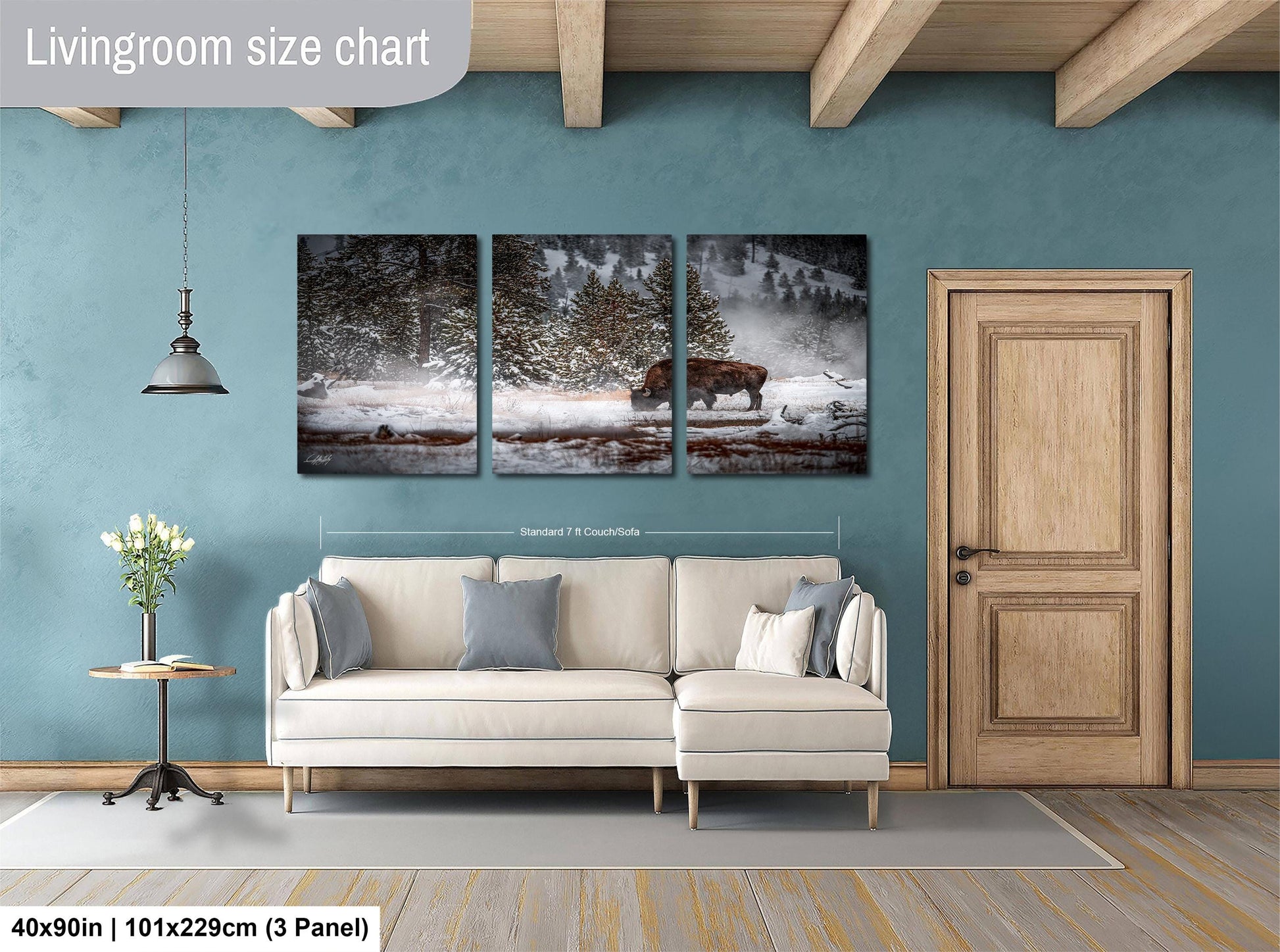 The image is a living room with a large painting of a snowy landscape featuring a bison in the center. The painting is mounted on the wall above a white sofa and a wooden door.