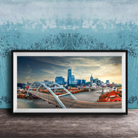 A framed photograph of a city skyline with a large bridge spanning a river, set against a blue sky with clouds.