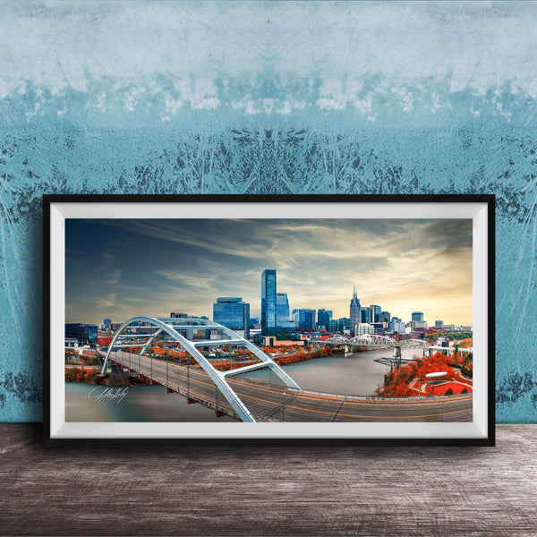 A framed photograph of a city skyline with a large bridge spanning a river, set against a blue sky with clouds.