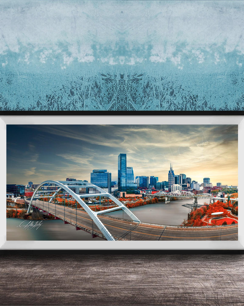 A framed photograph of a city skyline with a large bridge spanning a river, set against a blue sky with clouds.