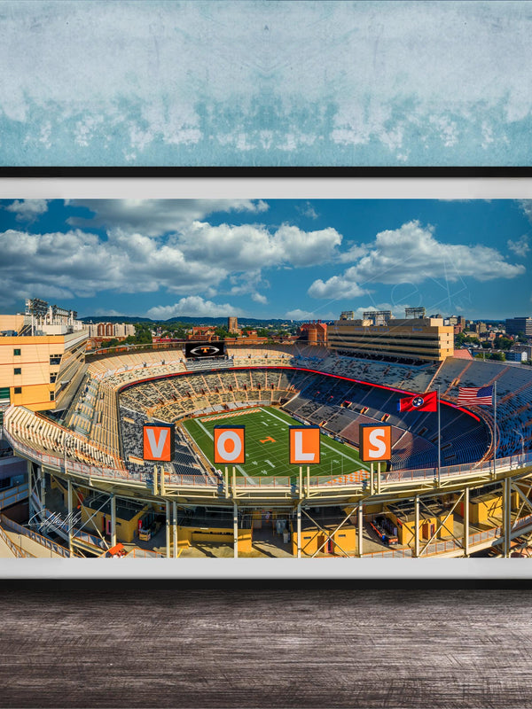 A framed photograph of a football stadium with the word "VOLS" prominently displayed, set against a blue sky with clouds.