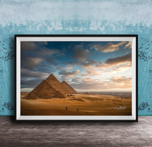 two large sandstone pyramids against a cloudy sky, with a few people walking in the foreground.