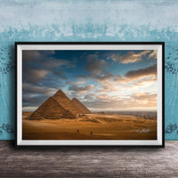 two large sandstone pyramids against a cloudy sky, with a few people walking in the foreground.