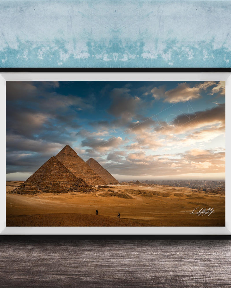 two large sandstone pyramids against a cloudy sky, with a few people walking in the foreground.