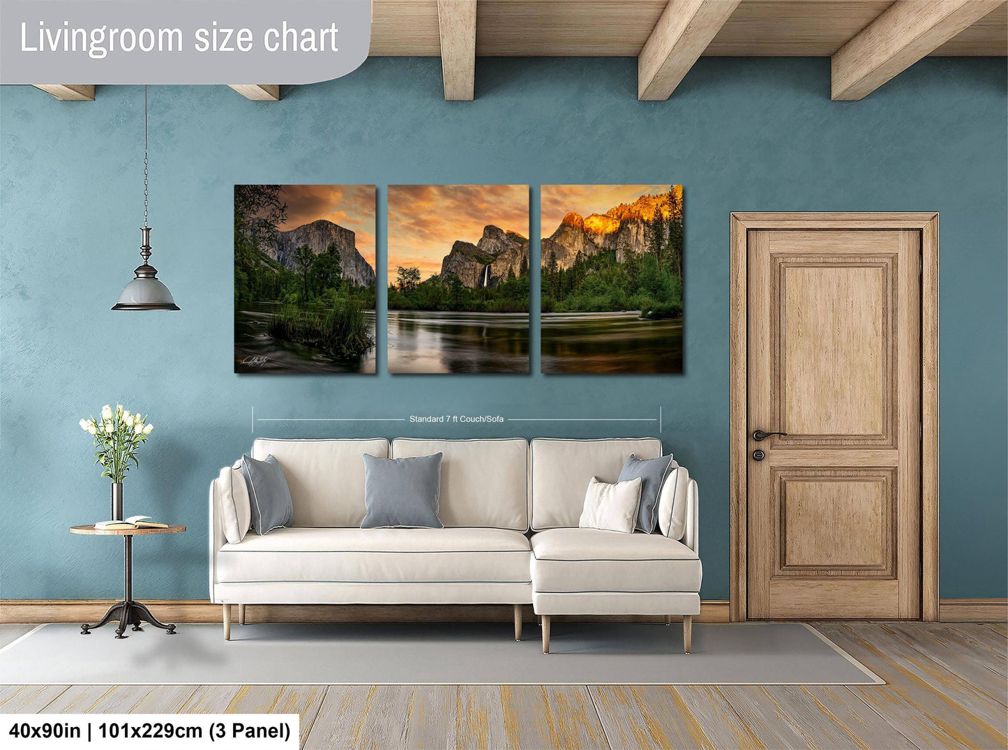 The image is a livingroom with a large wall art depicting a scenic landscape with mountains and a lake. The wall art is divided into three panels, each showcasing different aspects of the landscape. The living room has a white sofa and a wooden door, creating a cozy and inviting atmosphere.