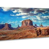 A cowboy on horseback stands in the foreground of a vast, arid desert landscape with towering rock formations and a blue sky with fluffy white clouds.