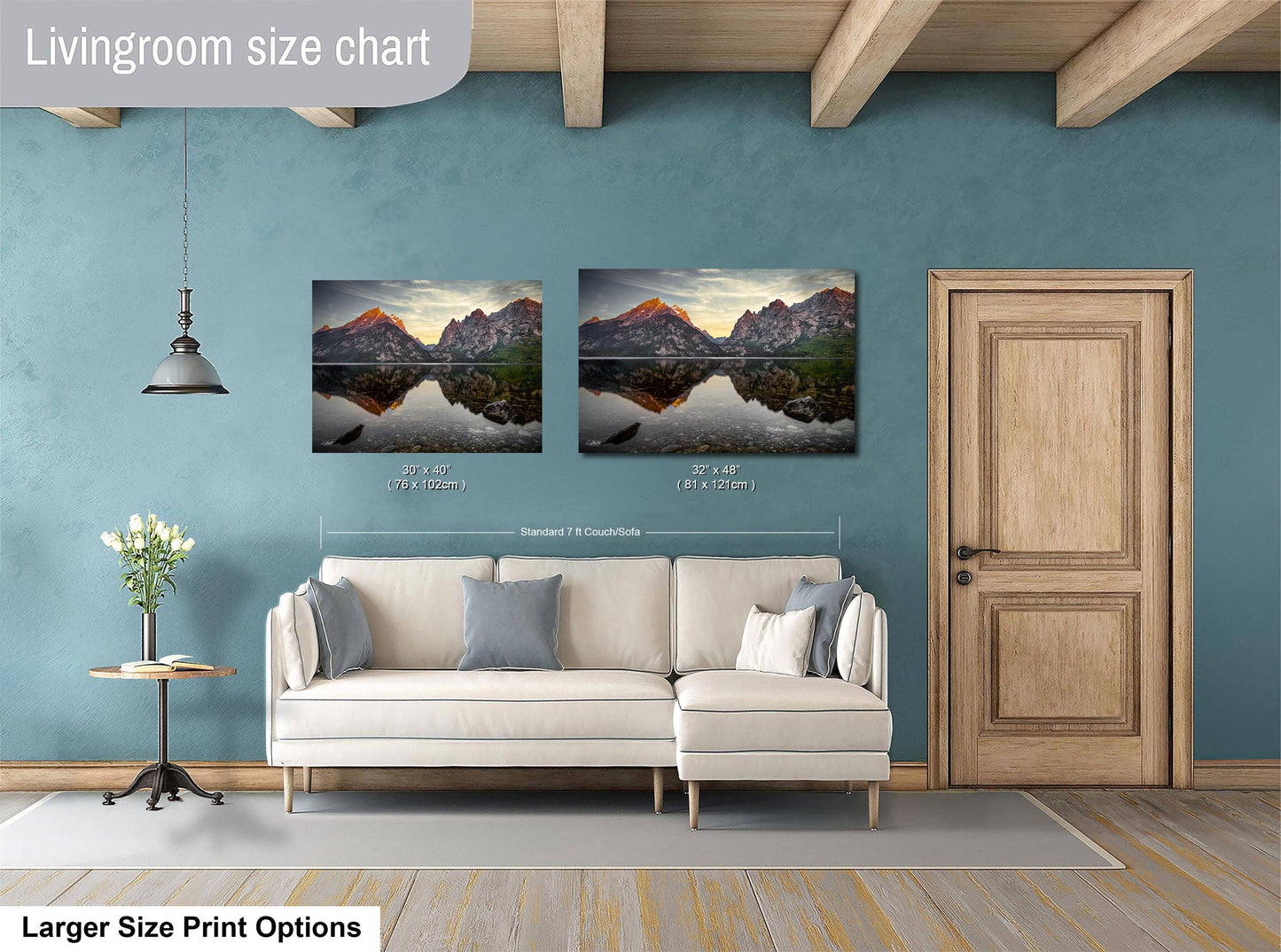 a living room with a white sofa and a wooden door. Above the sofa, there are two framed landscape paintings depicting mountains and a lake. The paintings are of similar size, with one being larger than the other. The living room has a blue wall and a wooden ceiling, creating a cozy and inviting atmosphere.