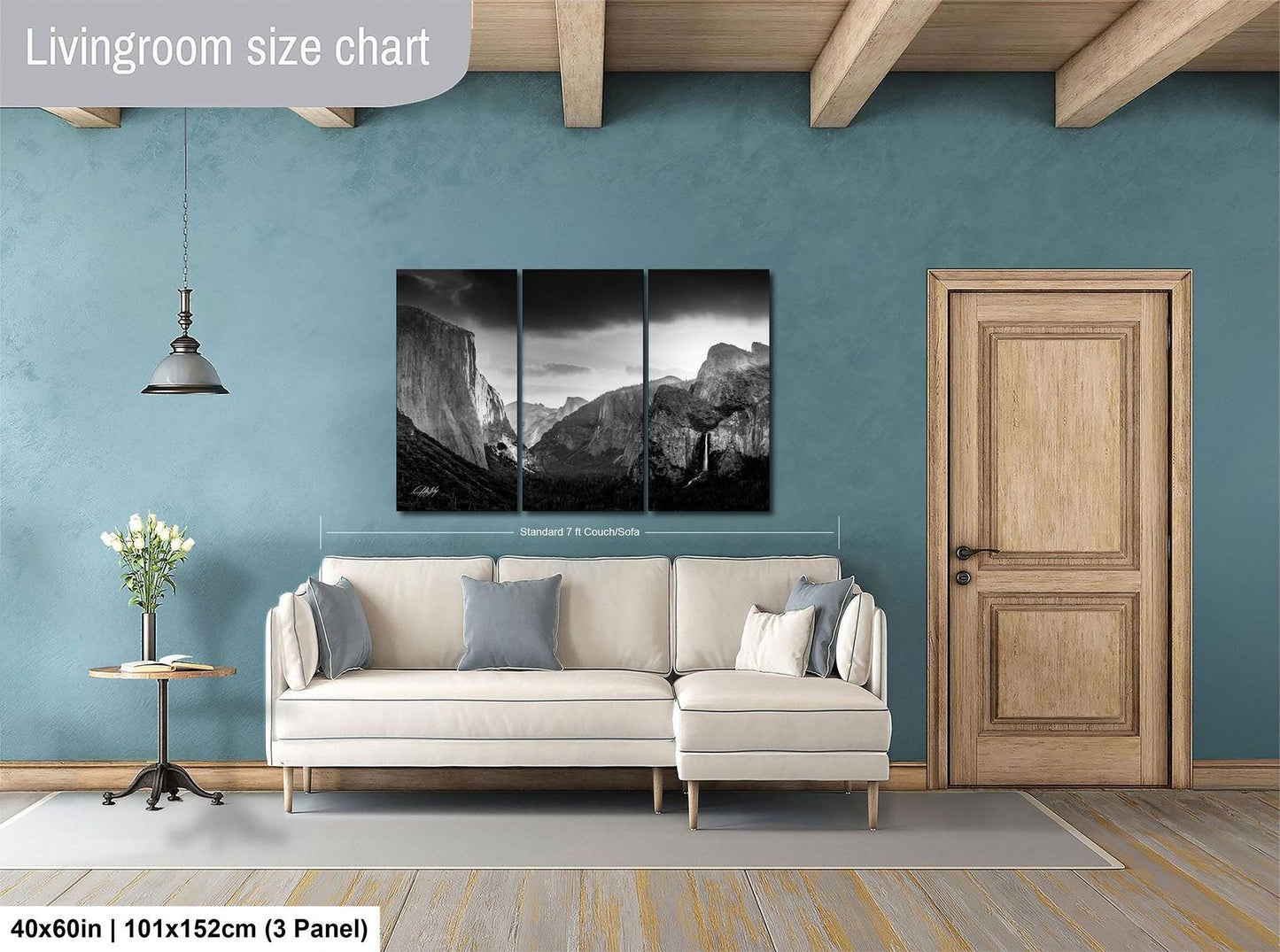 The image is a living room with a large, black and white landscape painting hanging on the wall above a white sofa. The painting is divided into three panels, and the living room has a wooden door and a small table with a vase of flowers.