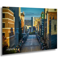 a city street lined with tall buildings, including a prominent sign for "Sterchi" and "TENNESSEE". The street is lined with flags and banners, creating a festive atmosphere. The sky is clear blue, and the sun is shining brightly, casting shadows and highlighting the architectural details of the buildings.