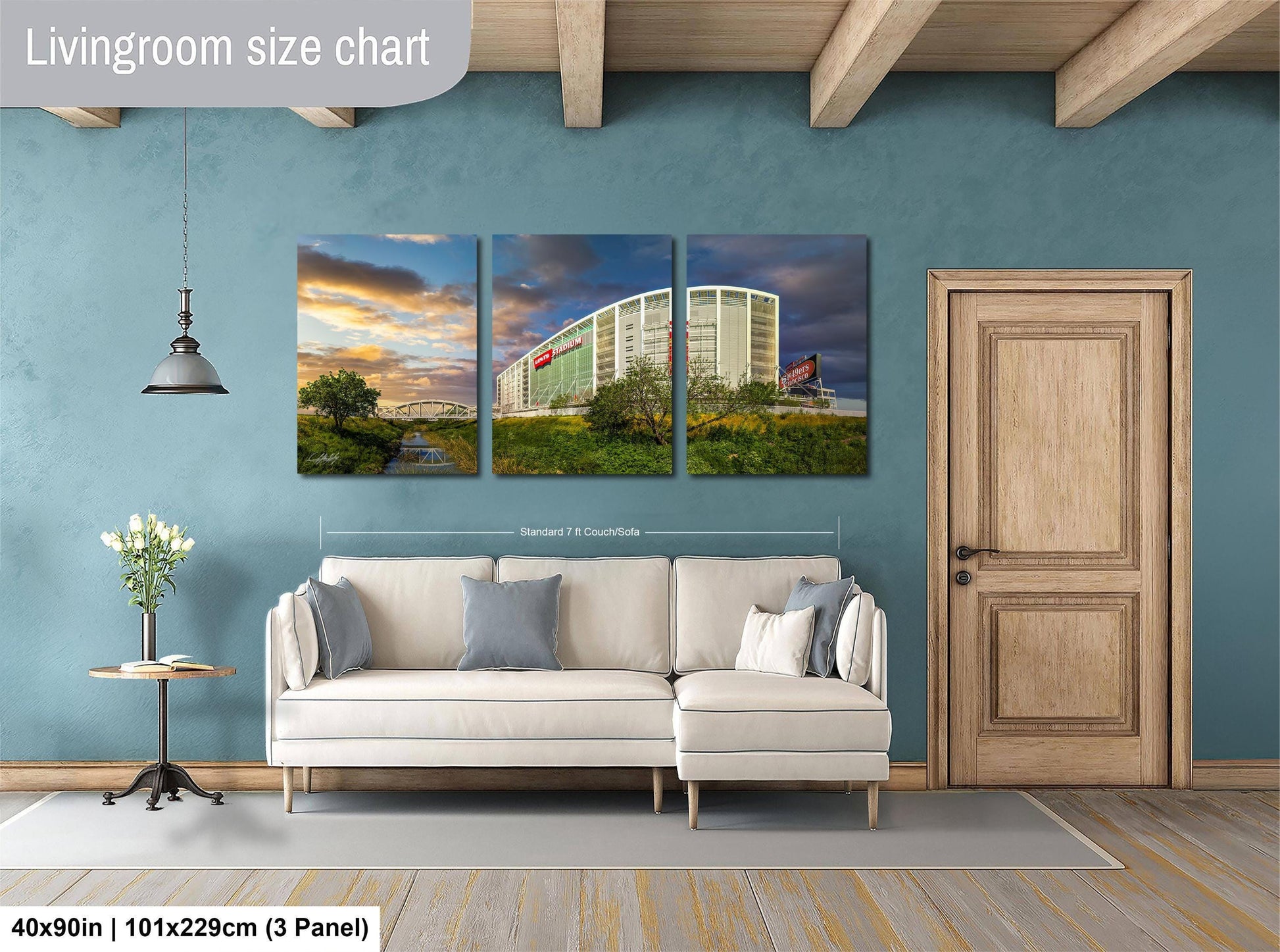 The image is a living room with a white sofa and a wooden door. Above the sofa, there is a large wall art collage depicting a building and a scenic landscape. The wall art is framed by a wooden border and is approximately 40 inches wide and 101.29 cm in height.