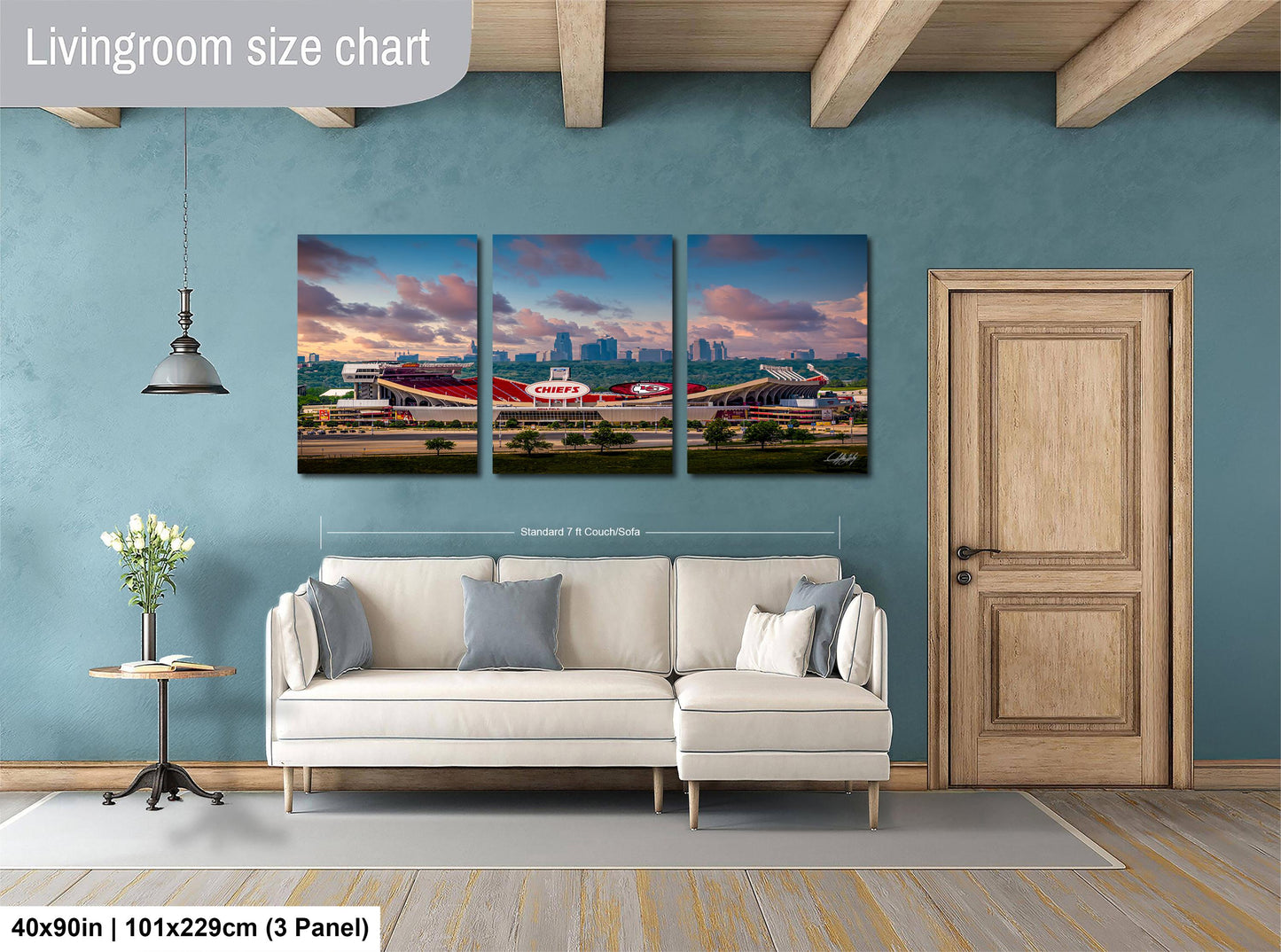 The image is a living room with a white sofa and a wooden door. Above the sofa, there is a large living room size chart that provides dimensions for the artwork. The artwork is a collage of three pictures depicting a city skyline at sunset.