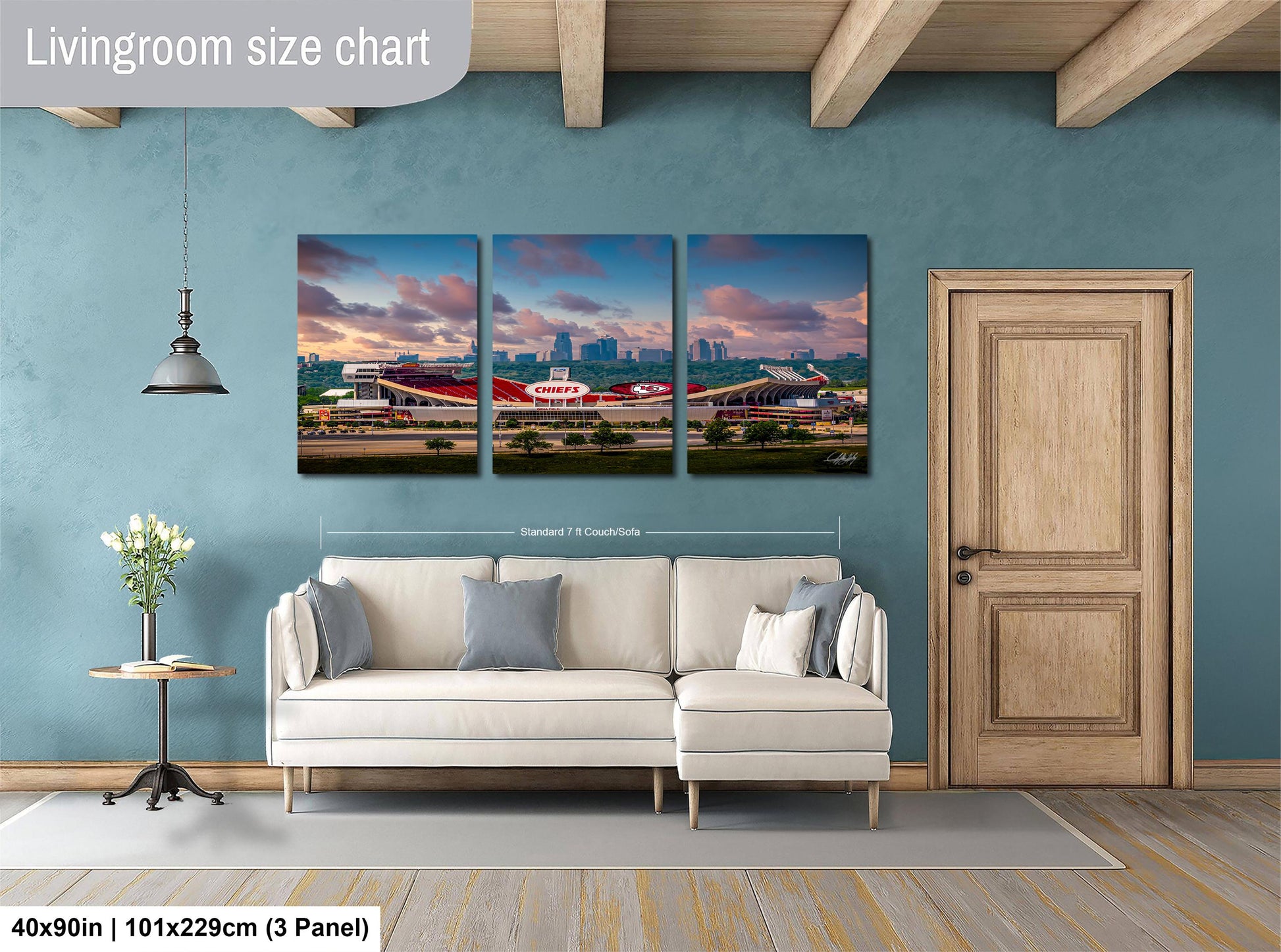 The image is a living room with a white sofa and a wooden door. Above the sofa, there is a large living room size chart that provides dimensions for the artwork. The artwork is a collage of three pictures depicting a city skyline at sunset.