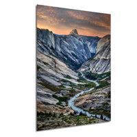 a breathtaking mountainous landscape with a winding river flowing through the valley. The sky above is a stunning display of orange and pink hues, creating a dramatic backdrop for the towering peaks. The photograph is a captivating representation of the natural beauty of the region, showcasing the grandeur of the mountains and the serenity of the river.