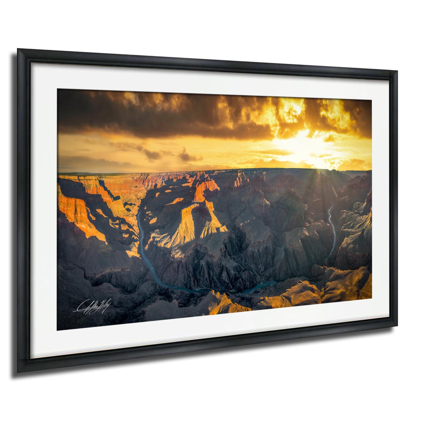 a breathtaking view of the Grand Canyon, with the sun setting behind the rugged, rocky landscape. The sky is filled with vibrant orange and yellow hues, creating a stunning backdrop for the canyon's dramatic features. The photograph is framed and displayed on a wall, showcasing the natural beauty of the scene.