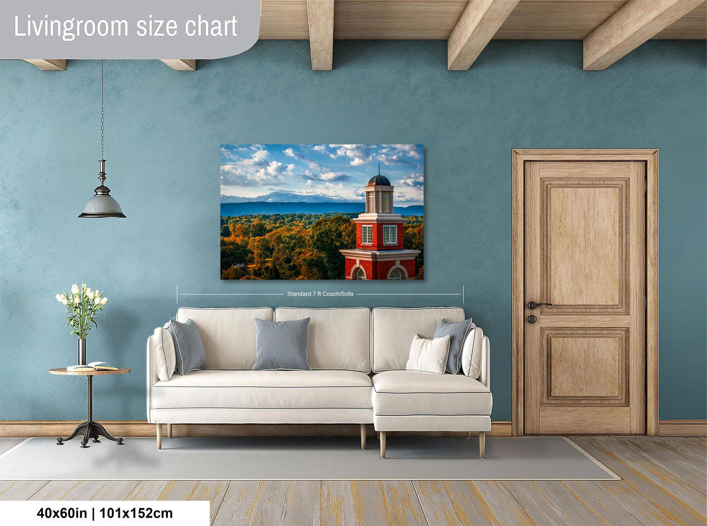 a living room with a large white sofa, a wooden door, and a painting of a red brick building with a tower on the wall.