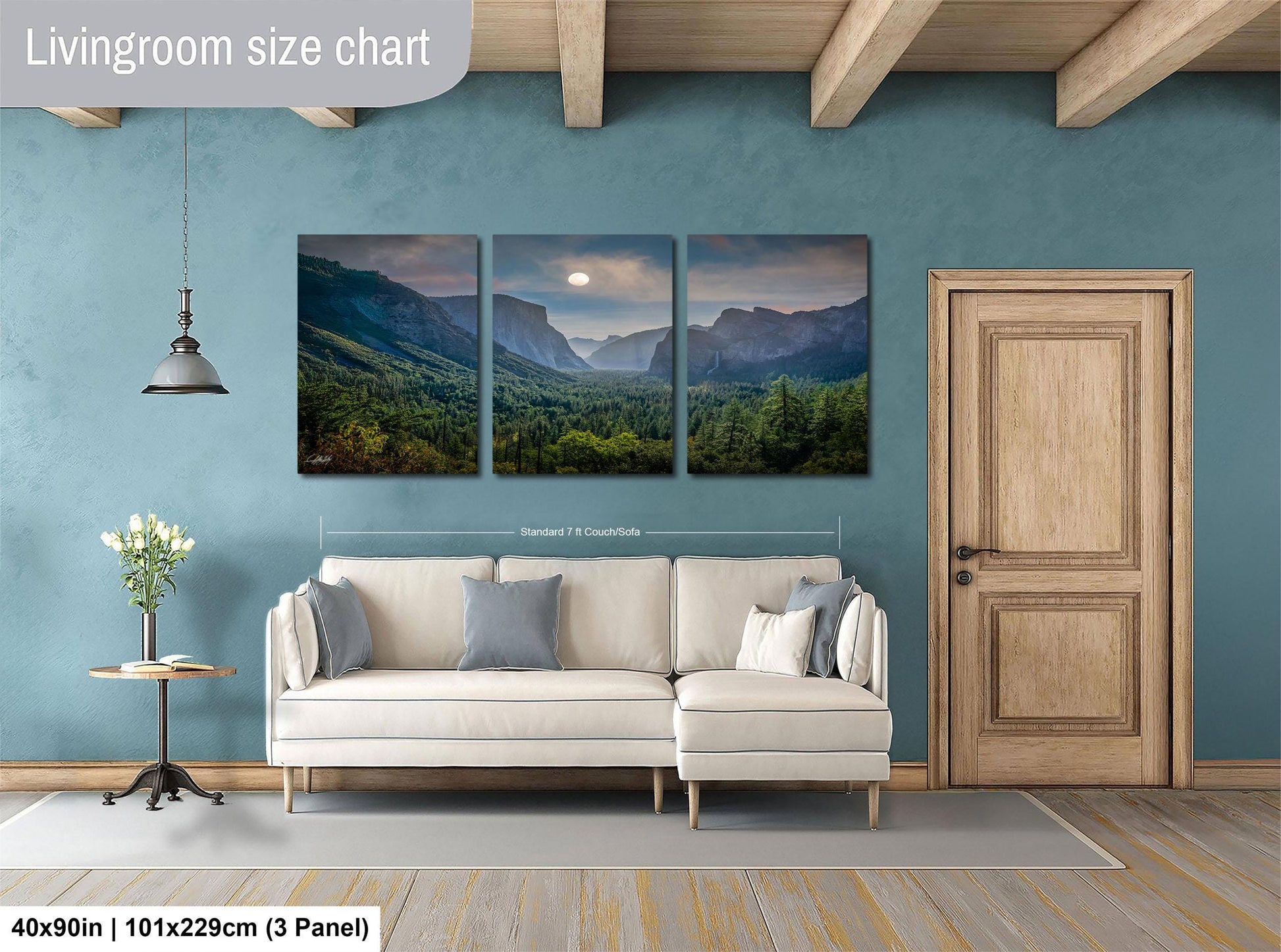 The image is a living room with a large, three-panel landscape painting hanging on the wall. The painting depicts a scenic mountain landscape with a full moon in the sky. The room has a white sofa and a wooden door, creating a cozy and inviting atmosphere.