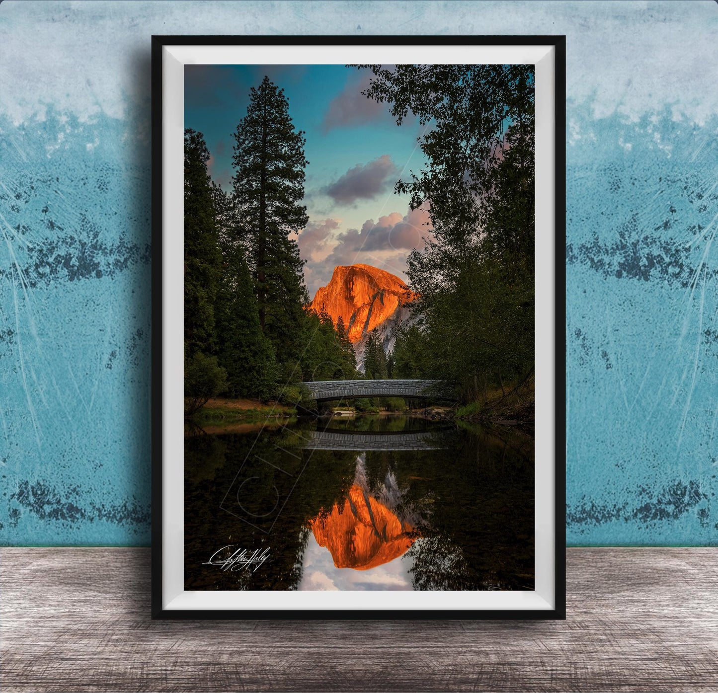 A framed photograph depicting a scenic landscape with a bridge, trees, and a mountain in the background, reflecting in a body of water.